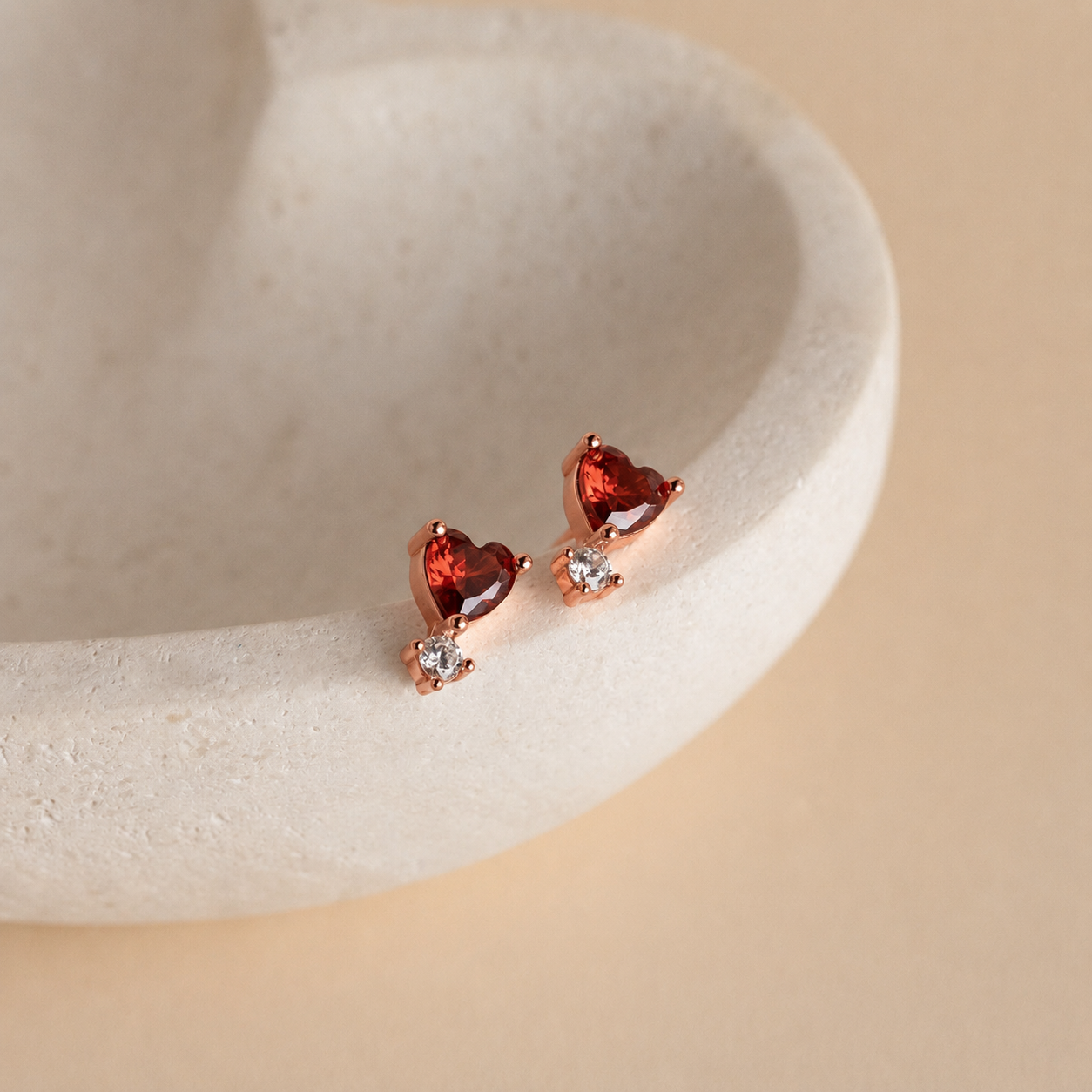 Heart-shaped gemstone earrings on a beige stone surface